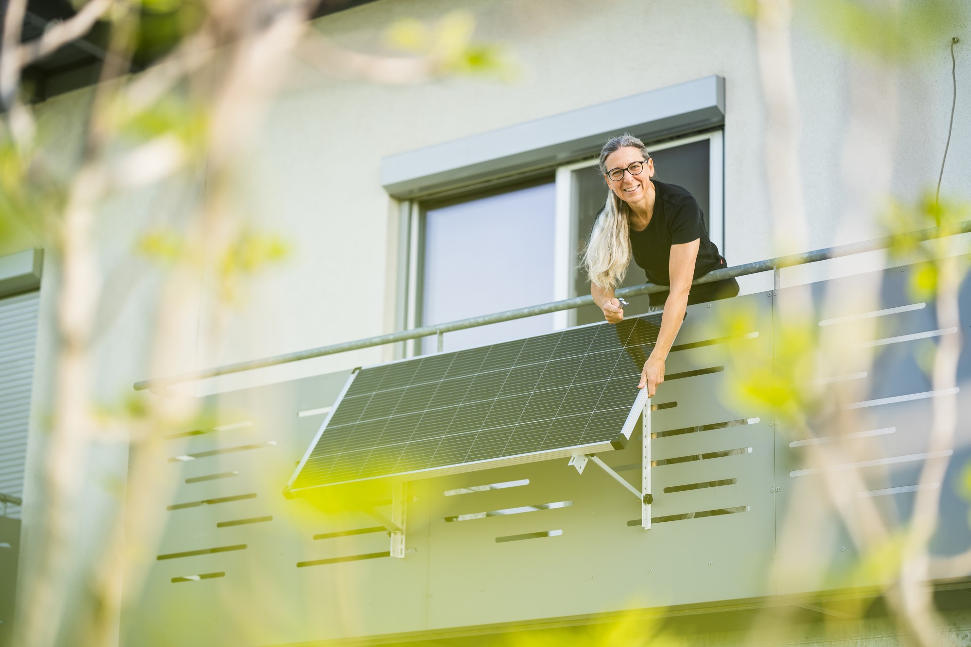 Eine glückliche Frau installiert ein Balkonkraftwerk an ihrem Balkon