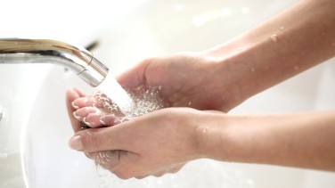 Ein Mensch steht vor der Spüle und füll ein Wasserglas aus dem Wasserhahn auf